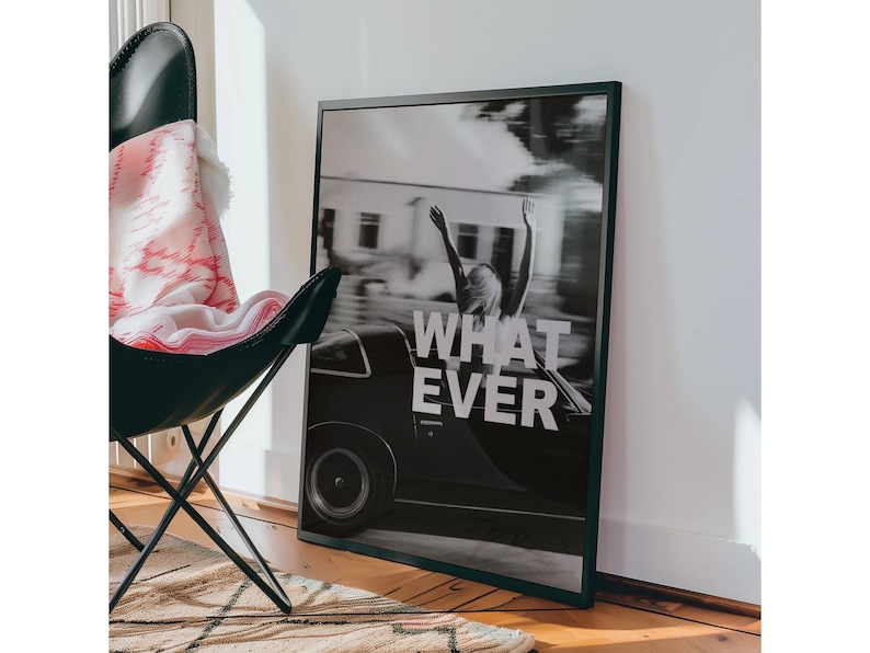 May include: Monochrome framed print showing a classic car and a person with raised arms, with the words "WHAT EVER". A black butterfly chair and a patterned blanket are in the foreground. The print is leaning against a white wall.