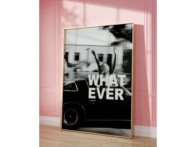 May include: Monochrome framed print showing a person with raised arms in a vintage car. The words "WHATEVER" are in white across the image. The print has a gold frame and is displayed against a pink wall, with a wooden floor.