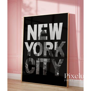 May include: A framed black and white print featuring the words "NEW YORK CITY" in large, bold letters. The letters are filled with a grayscale image of the city's skyline. The print is displayed in a room with pink walls.