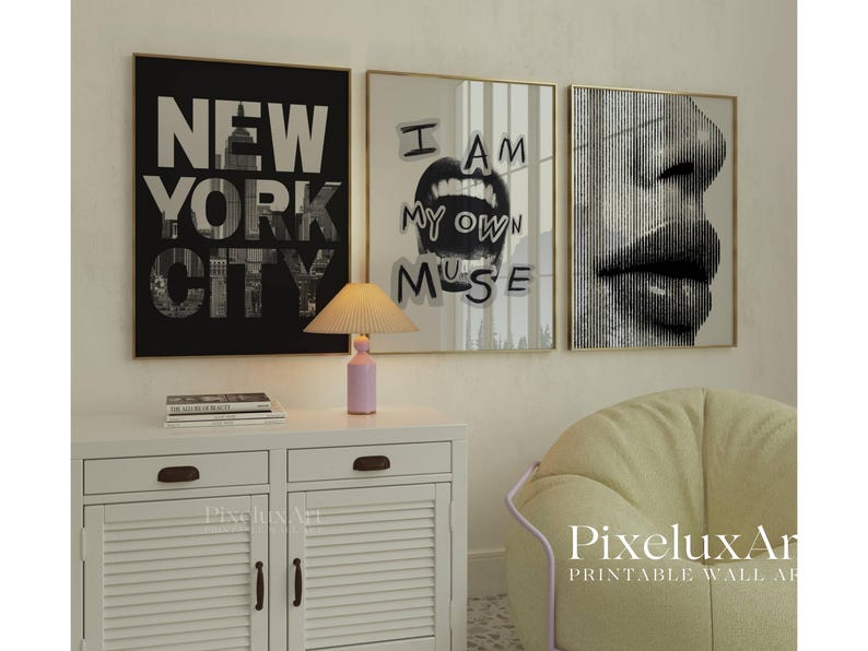 May include: Three framed wall art prints. The first is black and white with "NEW YORK CITY" text. The second says "I AM MY OWN MUSE". The third is a close-up of a face. A pink lamp sits on a white cabinet.