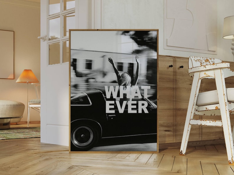 May include: Monochrome framed print showing a person with arms raised out of a classic car. The word "WHATEVER" is displayed in large white letters. The image is set in a room with a wooden floor and a distressed white chair.