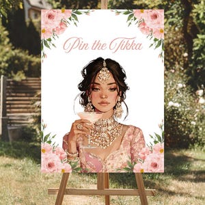 May include: A wooden easel displays a sign with the text "Pin the Tikka". The sign features an illustration of a woman in traditional Indian attire, holding a cocktail. Pink floral accents frame the image, set against a backdrop of greenery.
