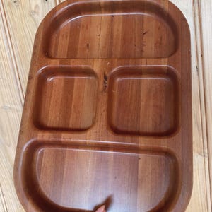 May include: A rectangular wooden serving tray with a smooth, polished finish and a warm brown colour. The tray features four distinct compartments: one large semi-circular section at the top, two square sections in the middle, and one large semi-circular section at the bottom.