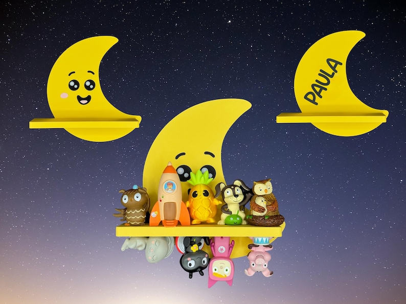 May include: Yellow crescent moon-shaped shelves with smiling faces and the name "Paula" on one. The shelves hold various colorful figurines, including an owl, rocket, pineapple, and other whimsical characters. The background is a starry night sky.