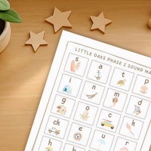 Puede incluir: Un "Little Oaks Phase 2 Sound Mat" impreso con letras e imágenes ilustradas, incluyendo una tabla de surf, un ancla, una tortuga y una concha. Estrellas de madera y pequeñas esferas de madera están dispersas sobre una superficie de madera.