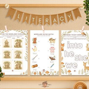 Op de afbeelding: Een houten educatieve display met drie bedrukte werkbladen. De werkbladen bevatten illustraties met bosmotieven en tekst voor lees- en schrijfactiviteiten. Een banner met de tekst "LITERACY" hangt erboven.
