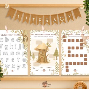 Op de afbeelding: Een educatieve display met houten frame met drie werkbladen. De bladen bevatten het traceren van letters, een activiteit voor het labelen van een paddenstoelenhuis en een letterpadspel. De banner hierboven luidt "LITERACY". Het thema is ge&iuml;nspireerd op de natuur.