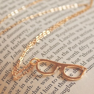 May include: A gold necklace with a pair of glasses charm. The necklace is laying on an open book with text. The text on the book reads "...was Bos's favorite and the Republicans..."