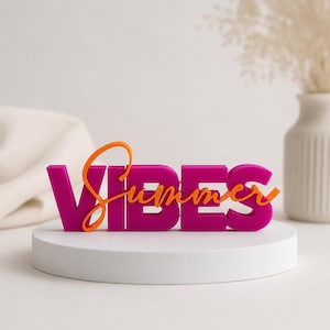 Könnte beinhalten: Ein magentafarbenes "VIBES"-Schild mit einem orangefarbenen "Summer"-Overlay, präsentiert auf einem weißen kreisförmigen Sockel. Das dekorative Schild steht vor einem neutralen Hintergrund mit einer Vase und Stoff.