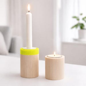 Pode incluir: Dois castiçais, um alto com uma vela branca e um detalhe amarelo néon, e outro mais curto com uma vela de chá acesa. Ambos são bege com detalhes canelados verticais, criando uma estética moderna e minimalista.