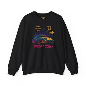 Könnte beinhalten: Schwarzes Sweatshirt mit einem Retro-Rennwagen-Motiv. Das Design zeigt ein blau-gelbes Auto mit dem Text "INSERT COIN" und einer Spieloberfläche mit Anzeige von Punktestand, Runde und Zeit. Das Sweatshirt hat einen Rundhalsausschnitt und lange Ärmel.