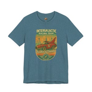 Può includere: T-shirt blu con un design retrò per l'"Intergalactic Racing Team". La grafica include un'auto da corsa rossa con il numero 16, sullo sfondo di un paesaggio urbano e le parole "Fuelled by Dreams".