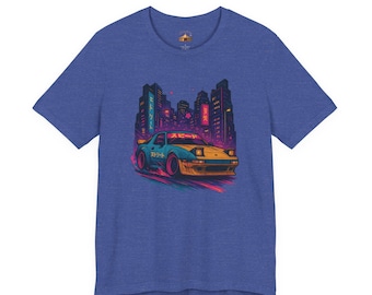 Könnte beinhalten: Blaues T-Shirt mit einer Grafik eines Retro-Sportwagens mit japanischem Text, vor einer neonbeleuchteten Stadtlandschaft. Das Auto ist gelb und blau, mit einem lebendigen, farbenfrohen Design. Das T-Shirt ist aus weichem Material.