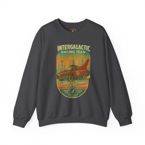 Könnte beinhalten: Dunkelgraues Sweatshirt mit Retro-Grafik. Das Design zeigt ein rotes Rennauto mit dem Text "INTERGALACTIC RACING TEAM" und "Fuelled by Dreams". Die Grafik enthält eine Stadtlandschaft und ein rundes Logo.