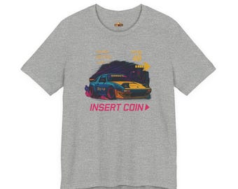 May include: A heather gray t-shirt featuring a retro-style illustration of a sports car with the text "INSERT COIN". The car is blue and yellow with a cityscape in the background.