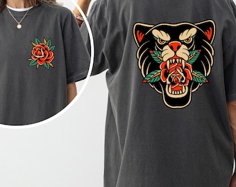 May include: Dark gray t-shirt featuring a rose graphic on the front and a panther head with a rose in its mouth on the back. The rose and panther head are in red, green, and yellow. The shirt is a short-sleeved, oversized style.