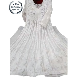 May include: A white, long-sleeved dress with intricate floral embroidery. The dress features a V-neckline and a flowing skirt. The image includes a "PREMIUM QUALITY" seal. The dress is made of a lightweight fabric.