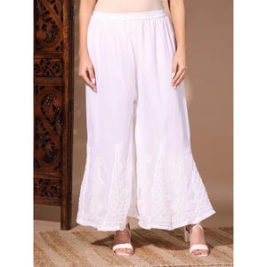 May include: White palazzo pants with embroidered floral detailing at the hem. The wide-leg pants are made of a lightweight fabric and have an elastic waistband. The pants are paired with white heeled sandals.