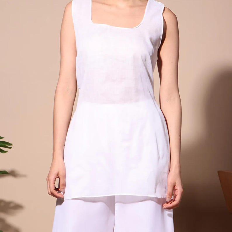 May include: A sleeveless white top with a square neckline. The top is paired with white pants. The clothing is made of a lightweight fabric, suitable for warm weather. The outfit is simple and elegant.