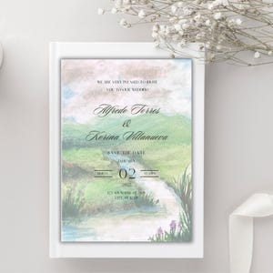 Op de afbeelding: Trouwkaart met een aquarel landschapsontwerp. De uitnodiging toont de namen "Alfredo Torres & Korina Villanueva" en de datum "02 maart 2022". De uitnodiging staat op een witte achtergrond.