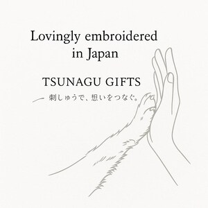 Puede incluir: Ilustraci&oacute;n gr&aacute;fica de una pata de perro tocando una mano humana. El texto dice "Lovingly embroidered in Japan" y "TSUNAGU GIFTS". Debajo hay texto en japon&eacute;s.