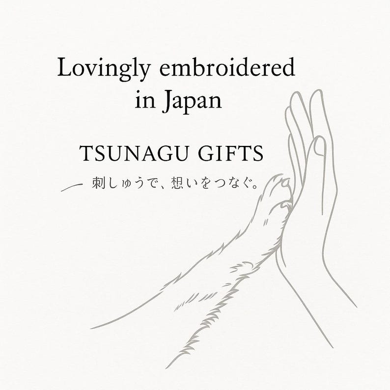 Puede incluir: Ilustraci&oacute;n gr&aacute;fica de una pata de perro tocando una mano humana. El texto dice "Lovingly embroidered in Japan" y "TSUNAGU GIFTS". Debajo hay texto en japon&eacute;s.
