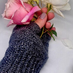 K&ouml;nnte beinhalten: Ein dunkelgrauer fingerloser Handschuh mit silbernen Sprenkeln, der einen Strau&szlig; rosa und wei&szlig;er Rosen h&auml;lt. Der gestrickte Handschuh hat ein strukturiertes Aussehen, und die Rosen sind in voller Bl&uuml;te.