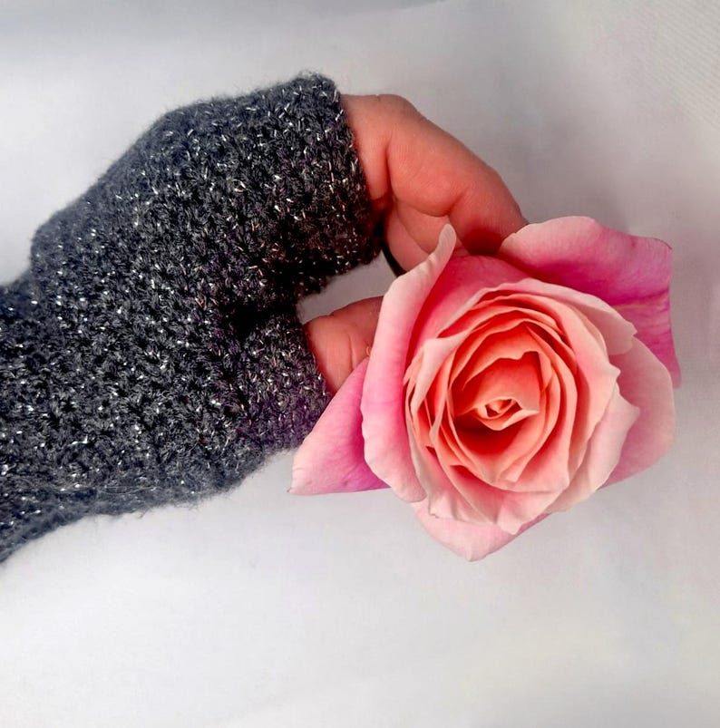 K&ouml;nnte beinhalten: Nahaufnahme eines grauen Fingerhandschuhs mit silbernen Sprenkeln, der eine rosa Rose h&auml;lt. Die Rose hat einen Farbverlauf von Rosat&ouml;nen, mit einem dunkleren Zentrum und helleren &auml;u&szlig;eren Bl&uuml;tenbl&auml;ttern. Der Hintergrund ist weiss.