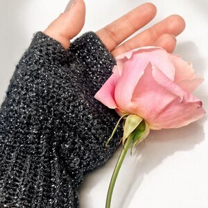 K&ouml;nnte beinhalten: Ein dunkelgrauer fingerloser Handschuh mit silbernen Sprenkeln wird gezeigt. Eine rosa Rose mit gr&uuml;nem Stiel und Bl&auml;ttern befindet sich neben dem Handschuh. Der Hintergrund ist wei&szlig;.