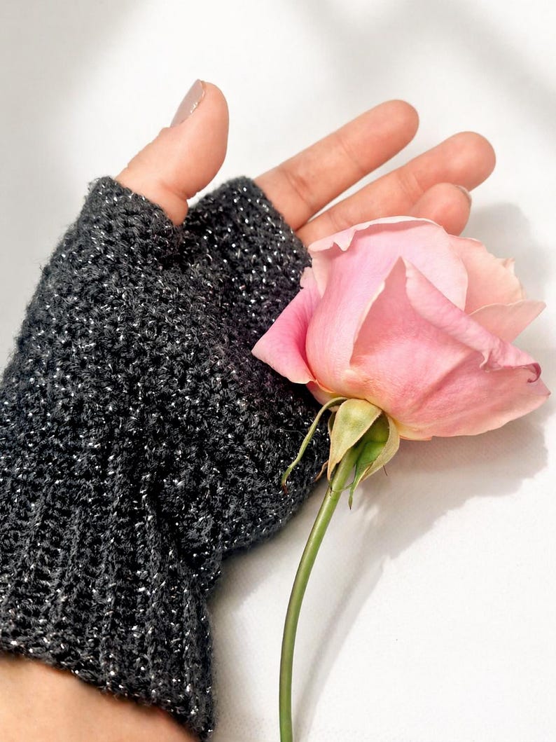 K&ouml;nnte beinhalten: Ein dunkelgrauer fingerloser Handschuh mit silbernen Sprenkeln wird gezeigt. Eine rosa Rose mit gr&uuml;nem Stiel und Bl&auml;ttern befindet sich neben dem Handschuh. Der Hintergrund ist wei&szlig;.