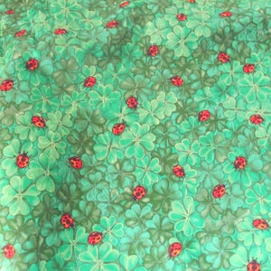 May include: A fabric pattern featuring a repeating design of green four-leaf clovers and red ladybugs. The ladybugs have black spots and are scattered across the clover background. The fabric has a slightly textured appearance.