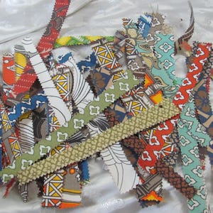 May include: A collection of long, narrow fabric strips featuring a variety of colorful patterns, including geometric shapes, floral motifs, and abstract designs in shades of red, blue, green, yellow, and white with pinked, zigzag-cut edges.