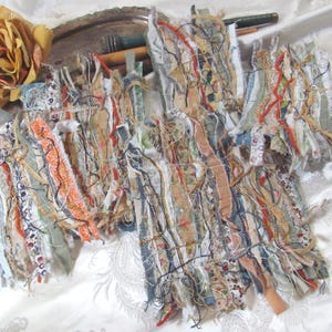 May include: A collection of rectangular fabric collages featuring layered strips of various textiles in shades of orange, green, blue, and cream. The pieces are embellished with intricate stitching, frayed edges, and loose threads, creating a textured surface with a multi-layered appearance.