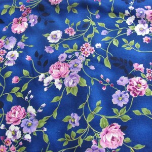 May include: A blue fabric with a floral pattern featuring pink and purple roses, small white flowers, and green leaves.