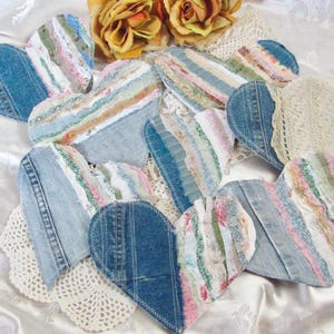 May include: A collection of heart-shaped ornaments crafted from blue denim fabric and layered with strips of multi-colored floral and patterned cotton textiles, featuring frayed edges and decorative lace accents on several pieces.