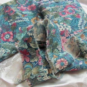 May include: Floral fabric with a teal background and a pattern of pink, red, and yellow flowers with green leaves. The fabric has a frayed edge, and is folded over on a white surface.