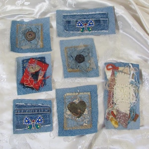 May include: A collection of seven rectangular denim fabric patches featuring various embellishments including dark buttons, a red fabric square, a dark green heart shape, and two blue butterfly motifs with white dots and yellow accents.
