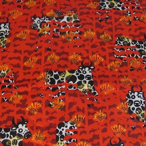 May include: Red fabric with a repeating pattern of black and white spotted cows and stylized yellow and orange floral elements. The cows have black horns and are set against a background of red vertical lines.