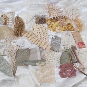 May include: An assortment of fabric pieces in cream, beige, and muted tones, featuring lace, crochet, and patterned textiles. The collection includes various shapes and sizes, suitable for crafting or mixed media projects. A variety of textures are visible.
