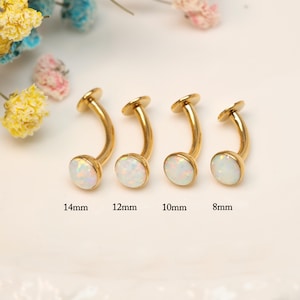 Pode incluir: Quatro piercings curvos dourados para sobrancelhas com pedras de opala branca. Tamanhos: 14 mm, 12 mm, 10 mm e 8 mm. As joias são exibidas em uma superfície branca com flores coloridas ao fundo.