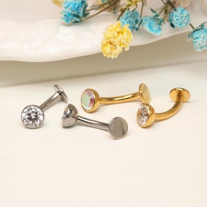 Puede incluir: Cinco piezas de joyería, incluyendo tres piezas curvas y dos rectas. Las piezas curvas son doradas, con una parte trasera redonda y plana y una gema en la parte delantera. Las piezas rectas son plateadas, con una parte trasera plana y una gema.