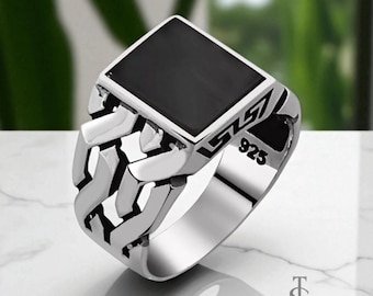 May include: A silver ring with a black square stone set in a silver frame. The ring has a chain-link design on the band. The ring is marked with "925". The ring is a piece of jewelry.