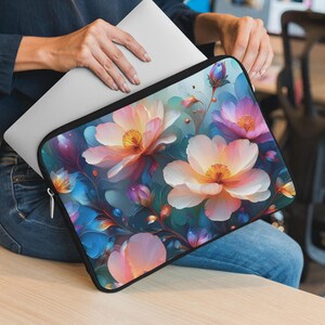 Könnte beinhalten: Eine Laptop-Hülle mit einem lebendigen Blumendesign. Das Muster zeigt große, stilisierte Blüten in Rosa, Pfirsich und Weiß vor einem Hintergrund in Blau- und Lilatönen. Die Hülle ist schwarz und enthält einen silbernen Laptop.