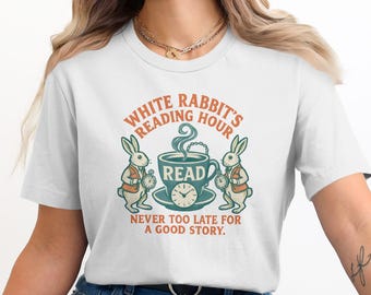 May include: White t-shirt featuring a whimsical design with the text "White Rabbit's Reading Hour." The graphic includes a teacup with the word "READ," two rabbits, and a clock. The phrase "Never too late for a good story" is also included.
