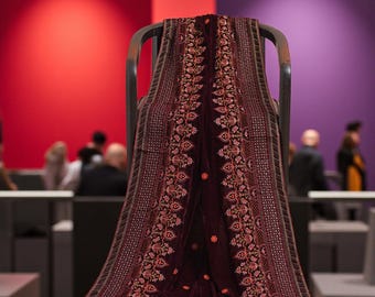 以下が含まれることがあります： 複雑な花の刺繍と詳細なボーダーが施された、バーガンディ色のベルベットのショールが椅子に掛けられています。ショールのデザインは、中央の花柄と装飾的なボーダーが特徴です。背景には赤と紫の壁があります。