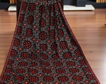 Puede incluir: Una manta estampada en tonos rojo oscuro y negro, sobre una silla de madera. La manta presenta un diseño floral repetido con acentos rojos y grises. Los bordes están acabados con un borde detallado.