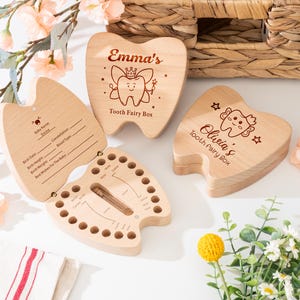 May include: Wooden tooth fairy boxes in the shape of teeth. One box is open, revealing a chart for baby teeth. Two boxes are closed, with the names "Emma's" and "Olivia's" engraved on them, along with the text "Tooth Fairy Box".