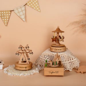 May include: Wooden music boxes featuring a Ferris wheel, carousel, and mountain scene. The Ferris wheel box is labeled "Peter", the carousel box is labeled "Emma", and the mountain scene box is labeled "Sophia". The boxes are made of light-colored wood.