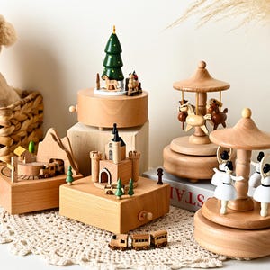 May include: A collection of wooden music boxes featuring various designs including a carousel with white ballerinas, a carousel with brown horses, a castle, a mountain landscape with a train, and a Christmas tree with small figures.