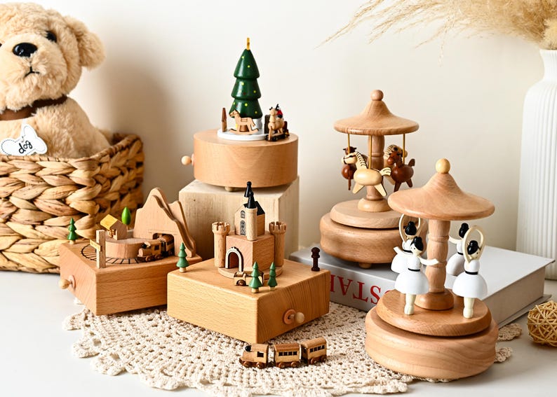 May include: A collection of wooden music boxes featuring various designs including a carousel with white ballerinas, a carousel with brown horses, a castle, a mountain landscape with a train, and a Christmas tree with small figures.